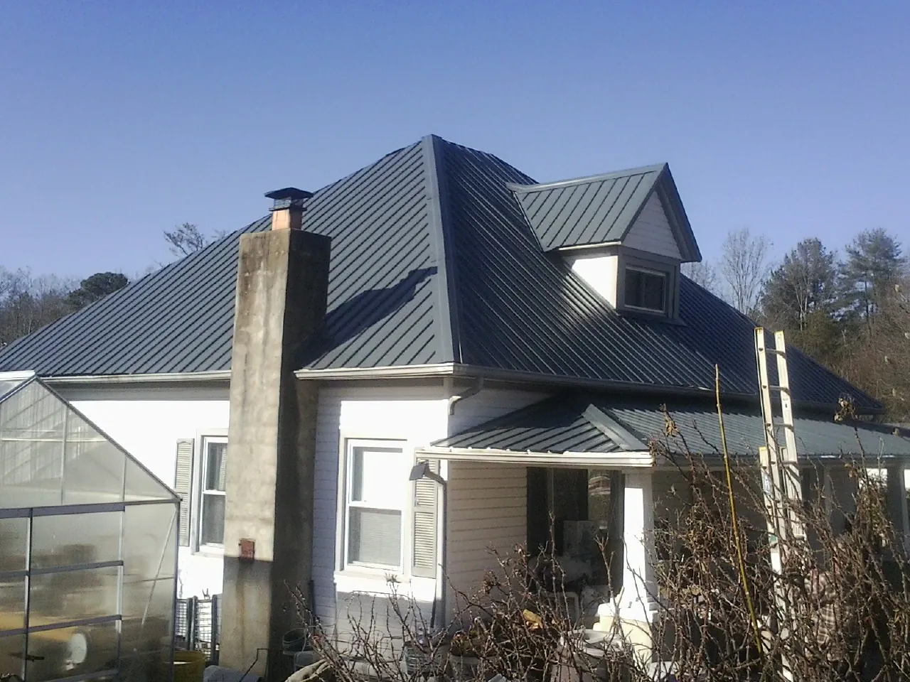 Dark blue standing seam metal roof on a white farmhouse with dormer — Slate & Tile Roof Repair by Roofing Brothers in College Corner