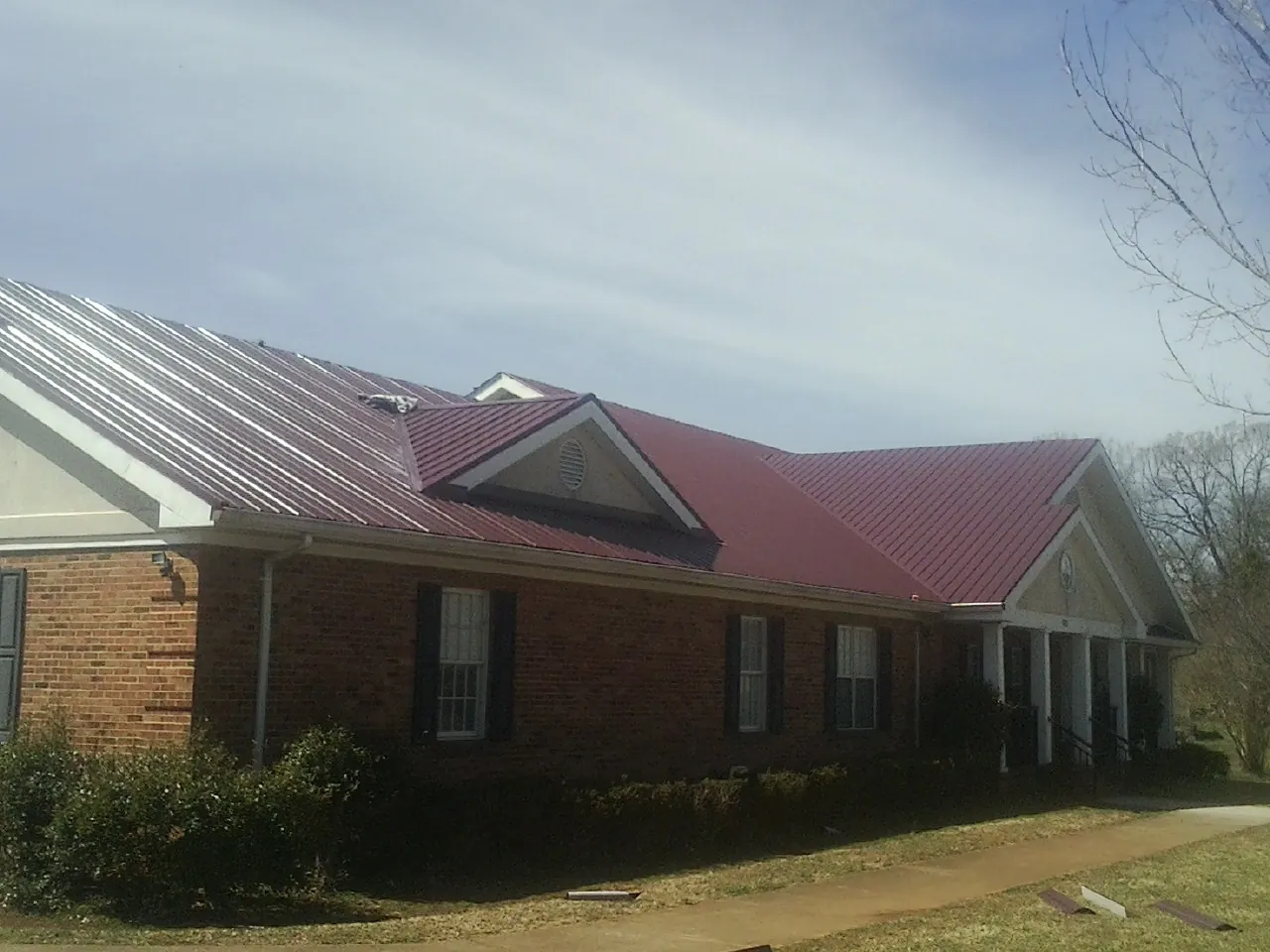 Red metal roof with gabled entries on a long brick building, from a Hail Damage Roof Repair job in College Corner