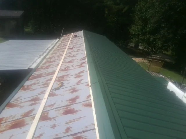 Old rusted panels beside newly installed green metal roofing — Wind Damage Roof Repair by Roofing Brothers in College Corner