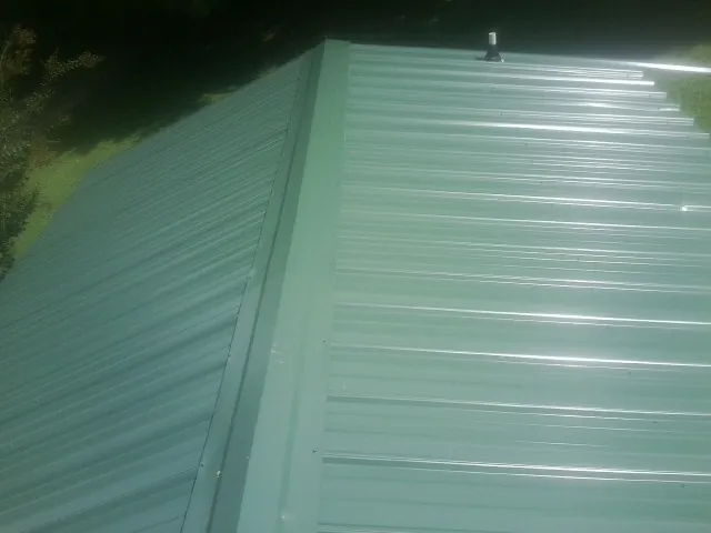 New green metal panels meeting at the ridge of a roof — Flat Roof Repair work by our crew in College Corner
