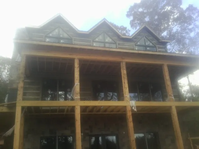 Dormers and porch framing on a large log home under construction — Roof Coating work by our crew in College Corner
