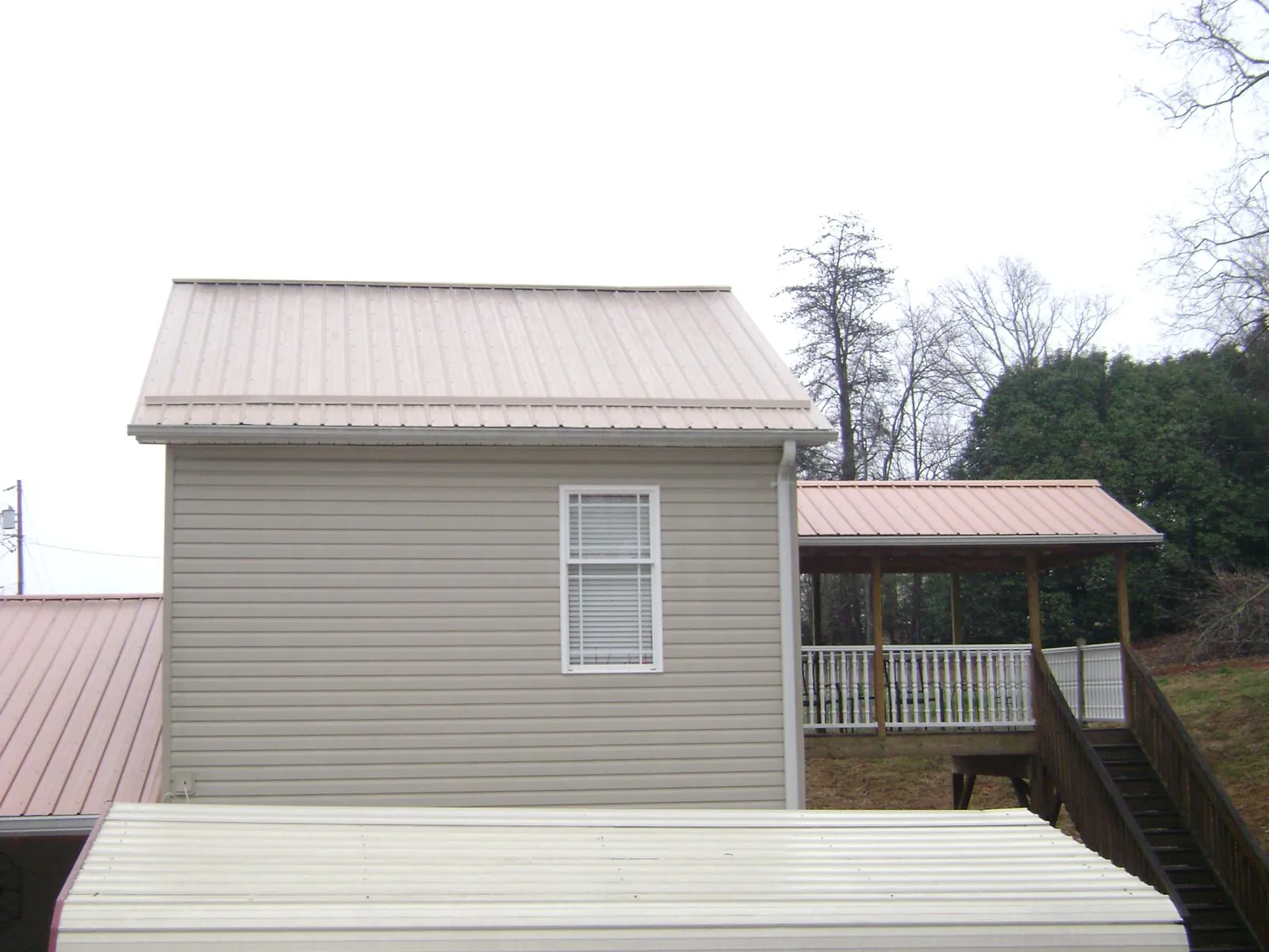 Tan metal roofs on a two story addition and attached porch, from a Roof Replacement job in College Corner
